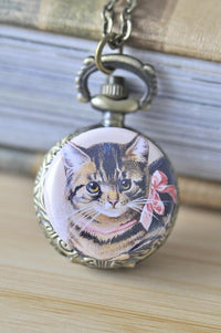 Close-up of vintage cat with pink bow pocket watch necklace pendant on bronze chain