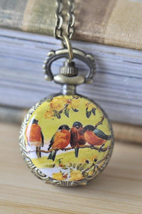 Bronze pocket watch necklace featuring four orange robins on a branch against a yellow floral background