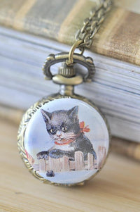 Bronze pocket watch necklace with vintage kitten and red ribbon illustration on a fence