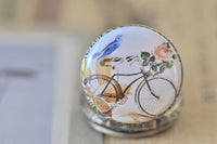 Close-up of bluebird perched on vintage bicycle with pink roses pocket watch design