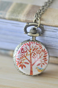 Pocket watch necklace with red tree and bird artwork on the case