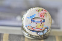 Close-up of bird and tea cup artwork on round pocket watch pendant with butterfly detail