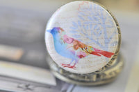 Close up of rainbow watercolour bird design on pocket watch necklace pendant