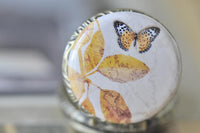 Close-up of pocket watch pendant artwork featuring an orange spotted butterfly on marbled gold leaves