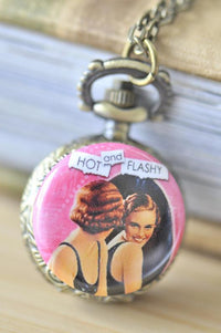 Close-up of pocket watch necklace pendant with retro pin up girls print and 'Hot and Flashy' text on pink background