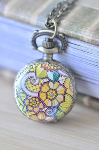 Close-up of floral ornament swirl pocket watch necklace pendant with yellow and pink mandala design