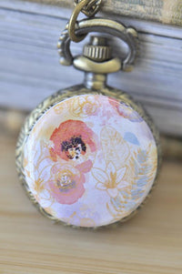 Close-up of pocket watch pendant with watercolour floral design in pink, coral and gold tones