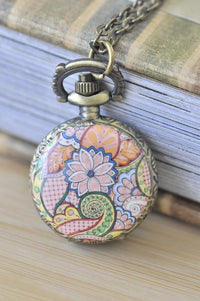 Close-up of floral paisley pocket watch necklace pendant resting against a stack of vintage books
