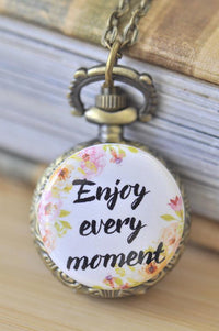 Close-up of bronze pocket watch pendant with floral "Enjoy every moment" quote cover on a chain