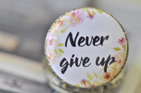 Top view of Never Give Up pocket watch pendant showing floral wreath and script text