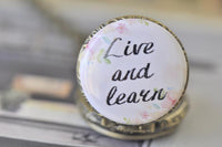 Detail of the 'Live and learn' script print surrounded by pastel watercolour flowers on the pocket watch pendant