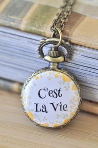 Bronze pocket watch necklace with C'est La Vie printed on a yellow floral background
