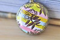 Close-up of pocket watch pendant featuring pink, yellow and blue striped floral design