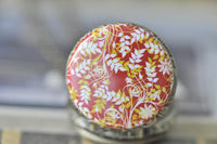 Close-up of red, white and yellow leaf pattern on pocket watch necklace lid