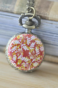 Antique bronze pocket watch necklace with red leaf and floral print lid, closed view