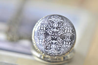Black and white floral pocket watch pendant resting closed on a chain