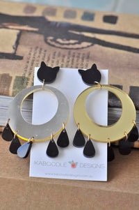Cat stud and mirrored gold hoop earrings with black teardrop charms, shown on card
