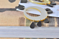 Close-up of gold Perspex hoop earring with black cat charm and teardrop fringe