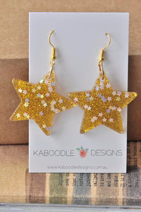 Pair of gold glitter resin star earrings with iridescent star flecks on Kaboodle card
