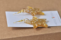 Gold glitter star earrings laid flat on Kaboodle Designs card, side angle