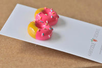 Close-up angled view of pink and yellow donut stud earrings showing glossy resin finish