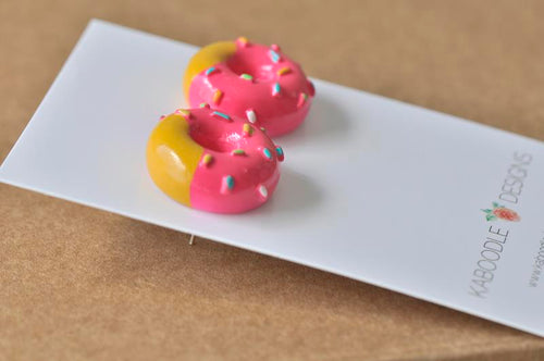 Close-up angled view of pink and yellow donut stud earrings showing glossy resin finish