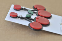 Angled close-up of cherry earrings showing red, black and green layered Perspex detail