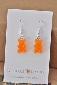 Pair of orange resin gummy bear earrings on white Kaboodle Designs card