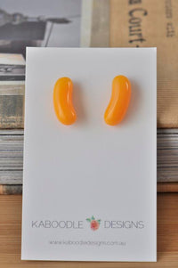 Pair of orange jelly bean shaped resin stud earrings on a white Kaboodle Designs card