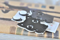 Close-up of black cat-shaped earrings resting on a stack of books, showing laser-cut detail and pin