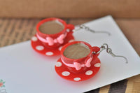 Close-up front view of two red teacup and saucer earrings with tea-filled cups