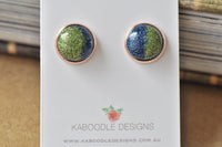 Pair of round rose gold stud earrings with blue and green glitter resin, on display card