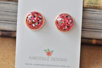 Round rose gold stud earrings with red, pink and silver glitter resin, shown on jewellery card