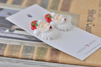 Close-up of resin Santa earrings on backing card resting on wooden surface