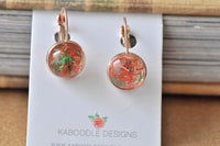 Two round resin dangle earrings with orange and green fleck detail on a Kaboodle Designs card