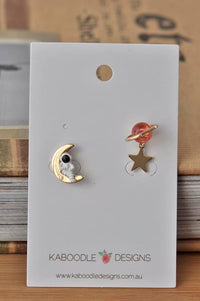 Mismatched astronaut moon and Saturn star stud earrings on Kaboodle Designs card