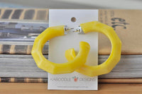 Front view of yellow faceted hoop earrings on card against striped book background