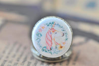 Close-up of boho unicorn artwork with pastel flowers on pocket watch pendant