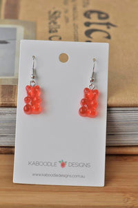 Red resin gummy bear dangle earrings displayed on white Kaboodle Designs card