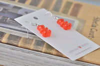 Pair of red gummy bear drop earrings on card resting against vintage books, angled view