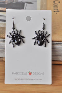 Pair of glossy black spider drop earrings on white Kaboodle Designs card, front view