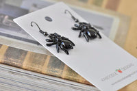 Black spider earrings on Kaboodle Designs card angled against stack of books