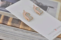 Pink unicorn stud earrings on card resting against stacked books
