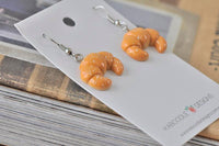 Close-up angled view of croissant earrings showing flaky resin detail and silver hooks