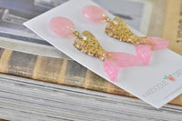Close-up of mermaid tail earrings resting on card showing resin glitter detail