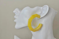 Close-up of yellow acrylic hoop earring worn on a mannequin ear