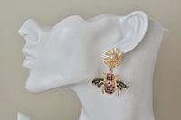 Close-up of rhinestone bee earring worn on ear, showing pink and green stone detail
