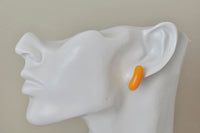 Orange jelly bean stud earring shown on ear for scale, side view