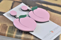 Close-up of two peach drop earrings laid flat showing glossy finish and leaf detail