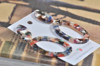 Pair of multicolour resin oval earrings laid flat showing glossy finish